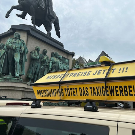 Auf einem gelben Sarg steht „Mindestpreise jetzt, Preisdumping tötet das Taxigewerbe“.