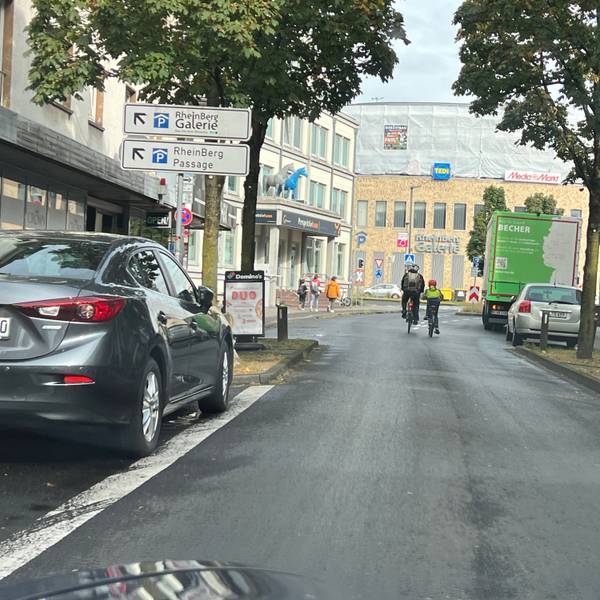 Zwei Radfahrer sind auf der unteren Hauptstraße in Richtung Schrankenkreisel und Rhein-Berg-Galerie unterwegs.