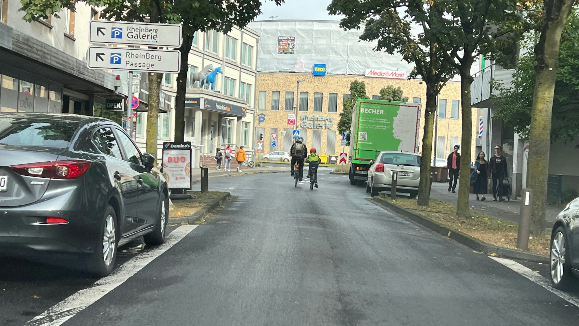 Zwei Radfahrer sind auf der unteren Hauptstraße in Richtung Schrankenkreisel und Rhein-Berg-Galerie unterwegs.