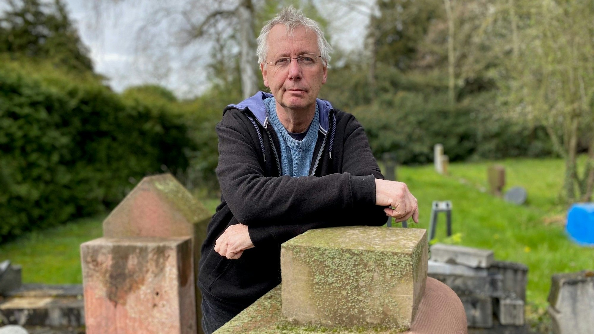 Zu sehen ist Hans-Jörg Blondiau, der sich auf einem Grabmal aufstützt.