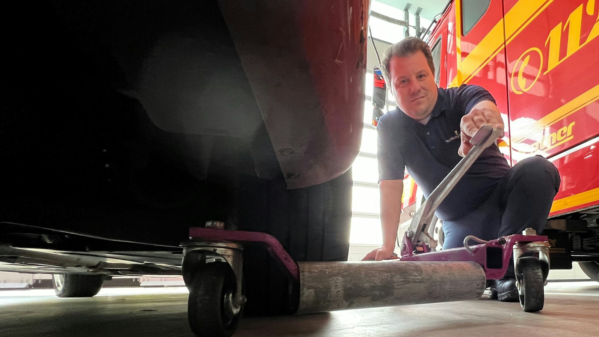 Auf dem Foto ist zu sehen, wie Feuerwehrmann Andreas Kirchharz einen Rangierwagenheber unter ein Auto schiebt.