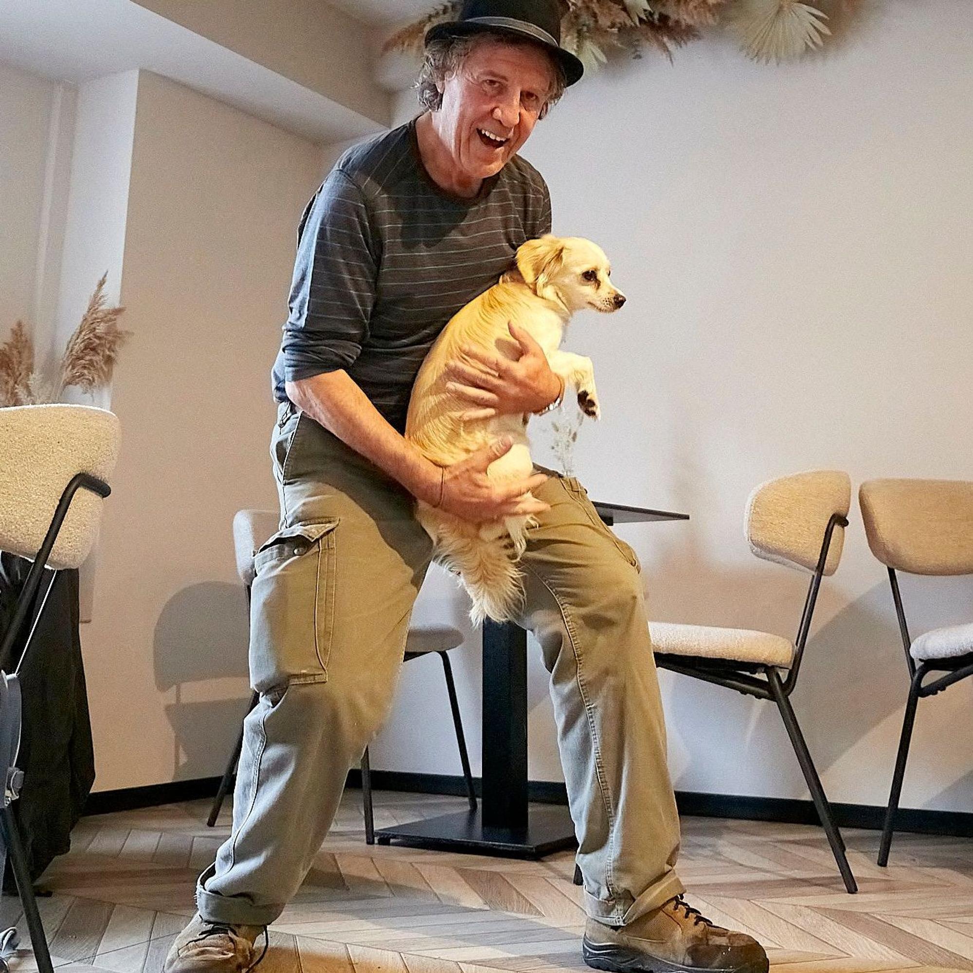 Norbert Scheuer trägt einen etwas zu kleinen Hut auf dem Kopf und einen Hund auf dem Arm.