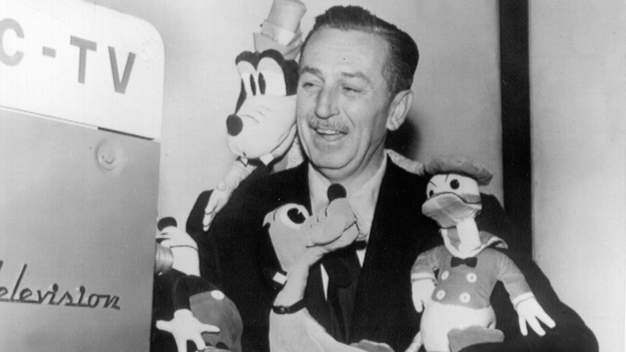 Der amerikanische Filmproduzent Walt Disney vor einer Fernsehkamera mit seinen Figuren Pluto (M) und Donald Duck (r) im Arm.