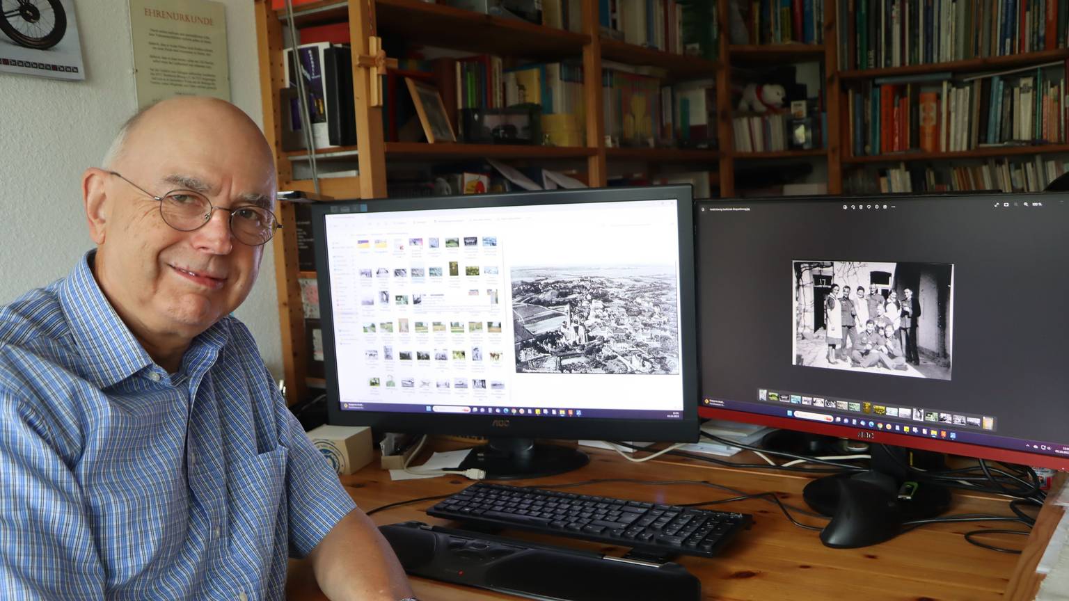Hans-Peter Schneider sitzt an seinem Schreibtisch in seiner Wahlheimat Swisttal vor zwei Computerbildschirmen mit Schwarz-Weiß-Fotos.