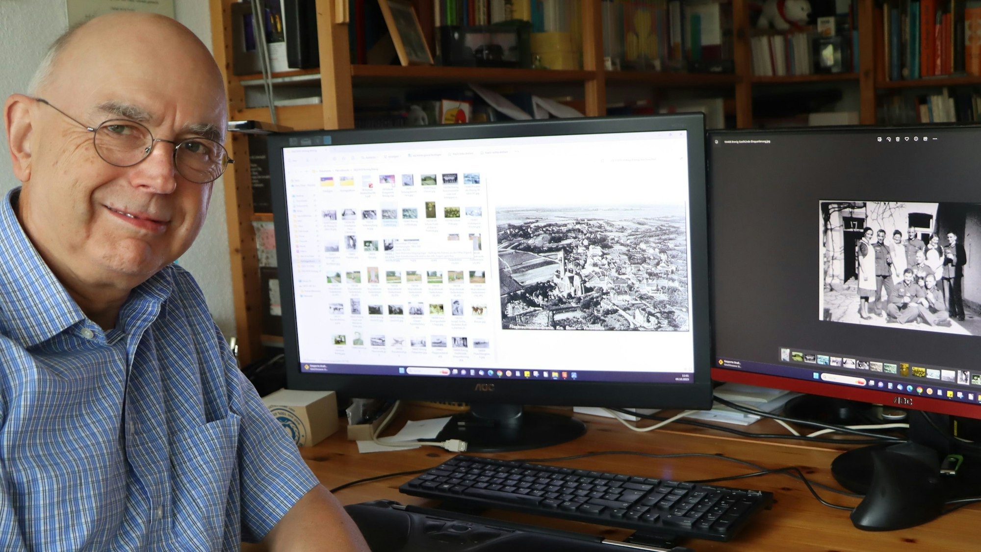 Hans-Peter Schneider sitzt an seinem Schreibtisch in seiner Wahlheimat Swisttal vor zwei Computerbildschirmen mit Schwarz-Weiß-Fotos.