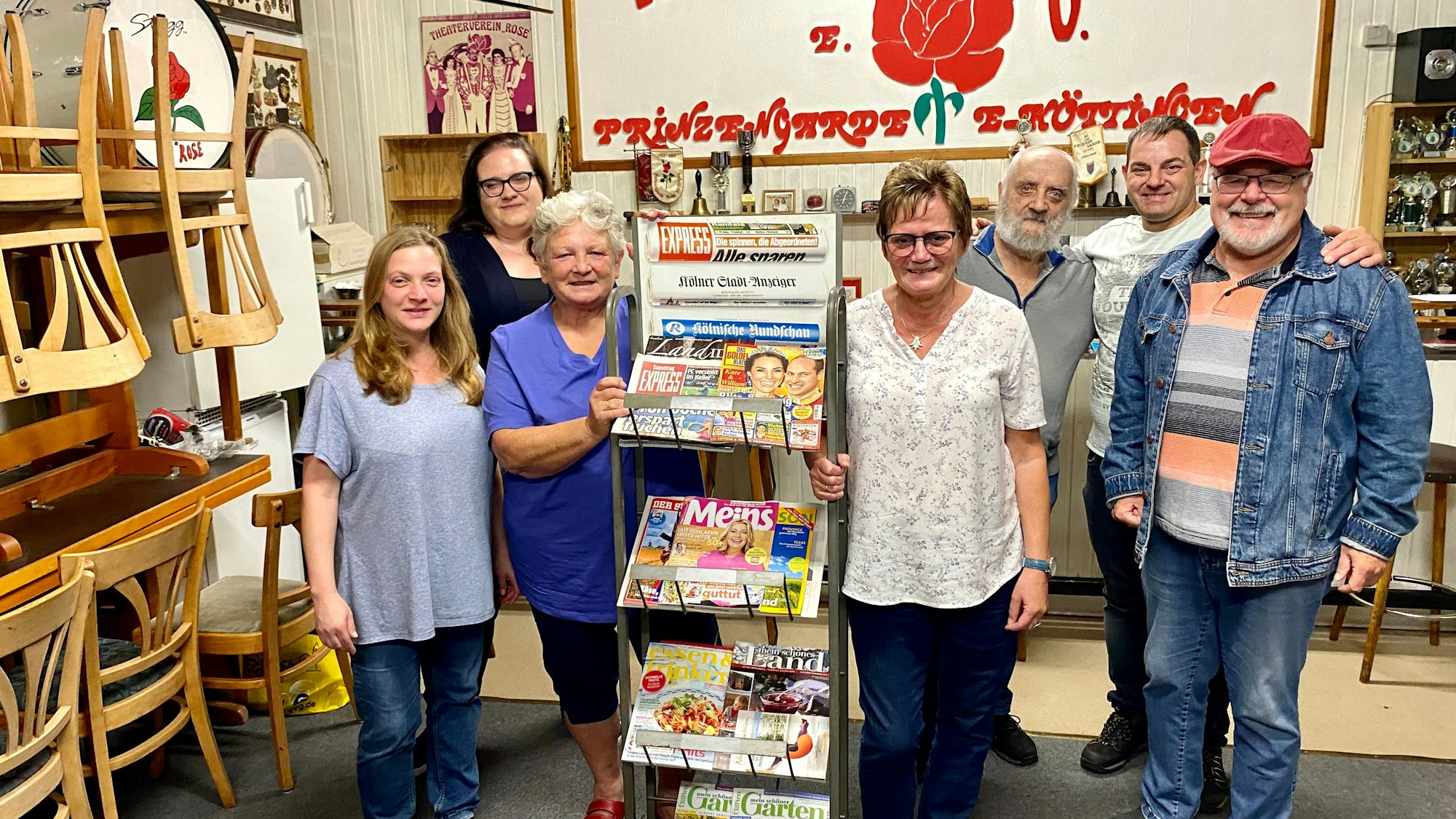 Sieben Leute sind um einen Zeitungsständer versammelt.