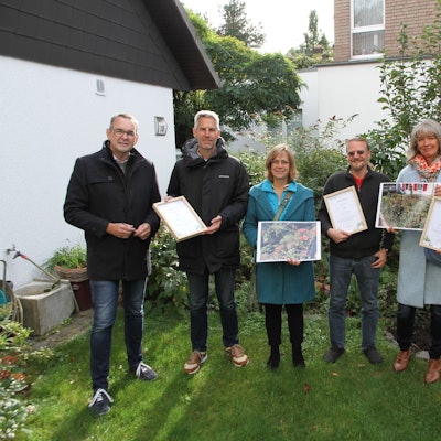 Drei Männer und drei Frauen stehen mit Fotos und Siegerurkunden in einem gepflegten Siegburger Garten