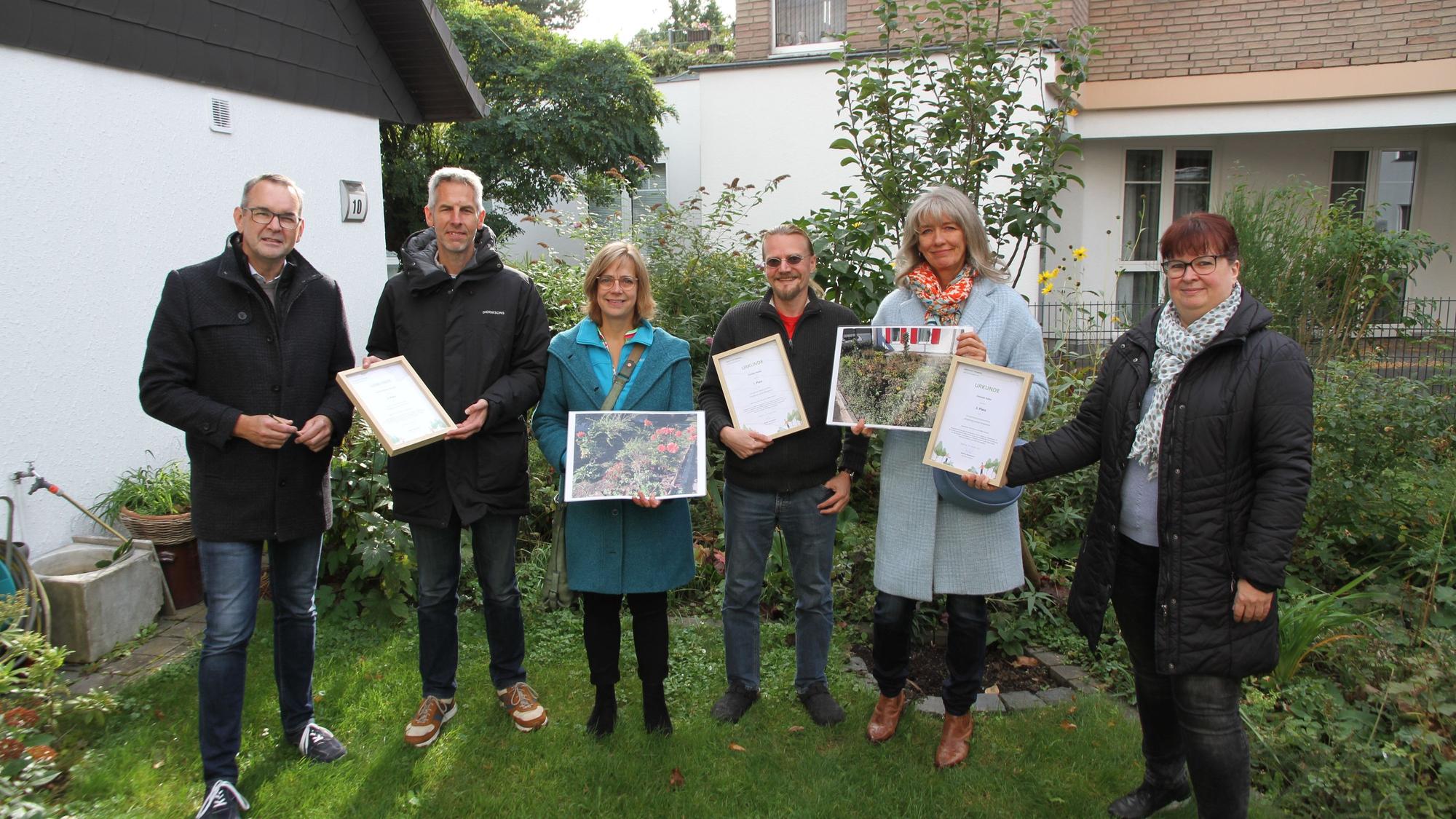 Drei Männer und drei Frauen stehen mit Fotos und Siegerurkunden in einem gepflegten Siegburger Garten