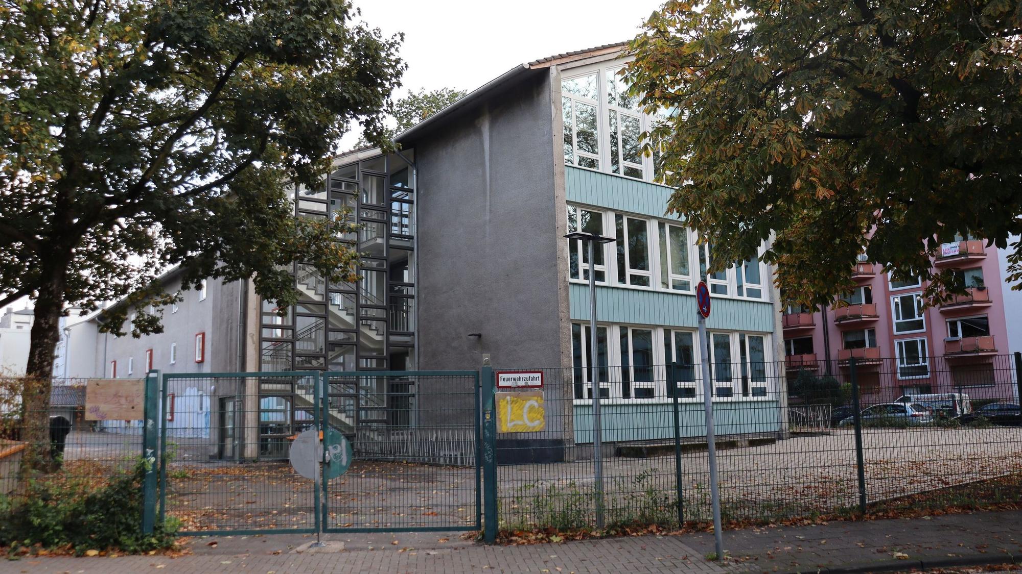 Hinter einem Zaun ist ein blau-graues Schulgebäude zu sehen.