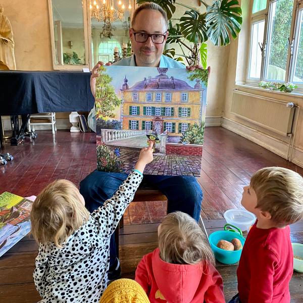 Der Autor hält eine Zeichnung in der Hand, auf der grüne Kobold vor einem prächtigen Gebäude zu sehen ist.