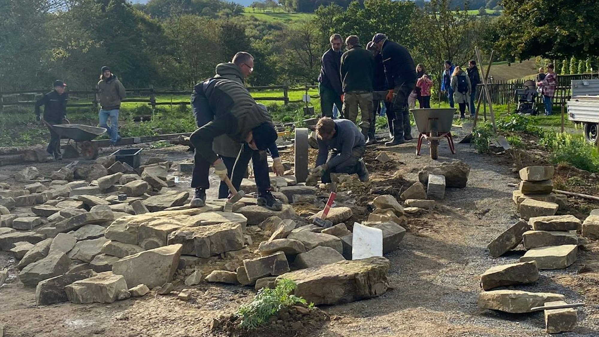 Menschen behauen große Grauwackesteine für eine Trockenmauer.
