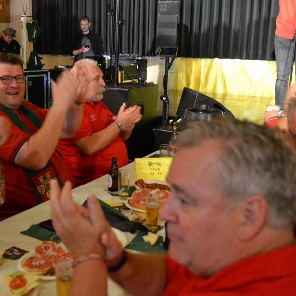 Einige Männer sitzen gut gelaunt am Tisch und klatschen zur Musik. Es gibt Bier und Mettbrötchen.