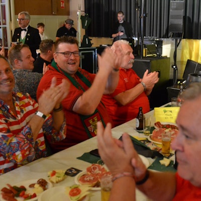 Einige Männer sitzen gut gelaunt am Tisch und klatschen zur Musik. Es gibt Bier und Mettbrötchen.