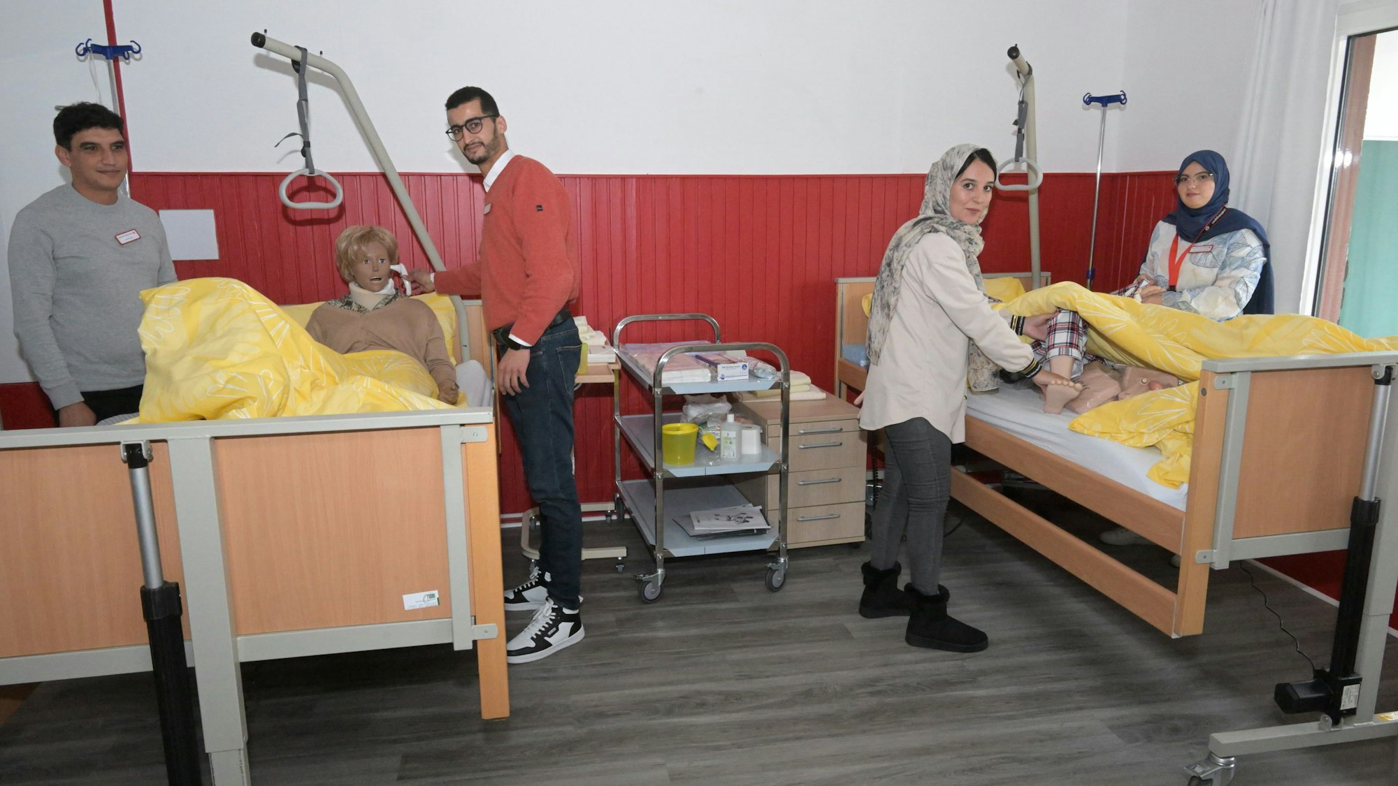 Angehende Pflegekräfte üben mit lebensgroßen Patientenpuppen in Pflegebetten ihren künftigen Berufsalltag.