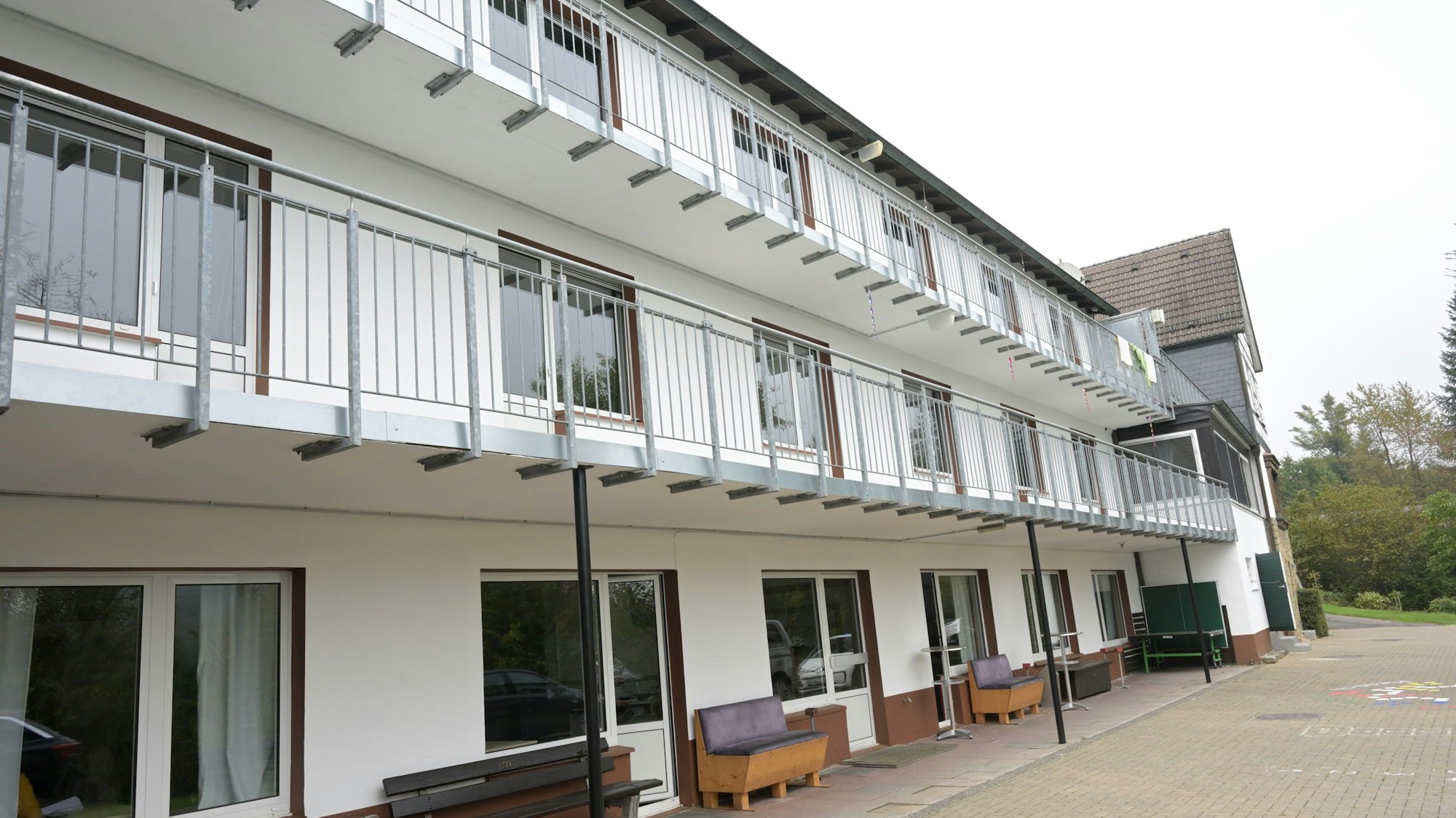 Auf dem Bild ist ein dreistöckiges Gebäude mit Balkonen und Terrasse zu sehen.