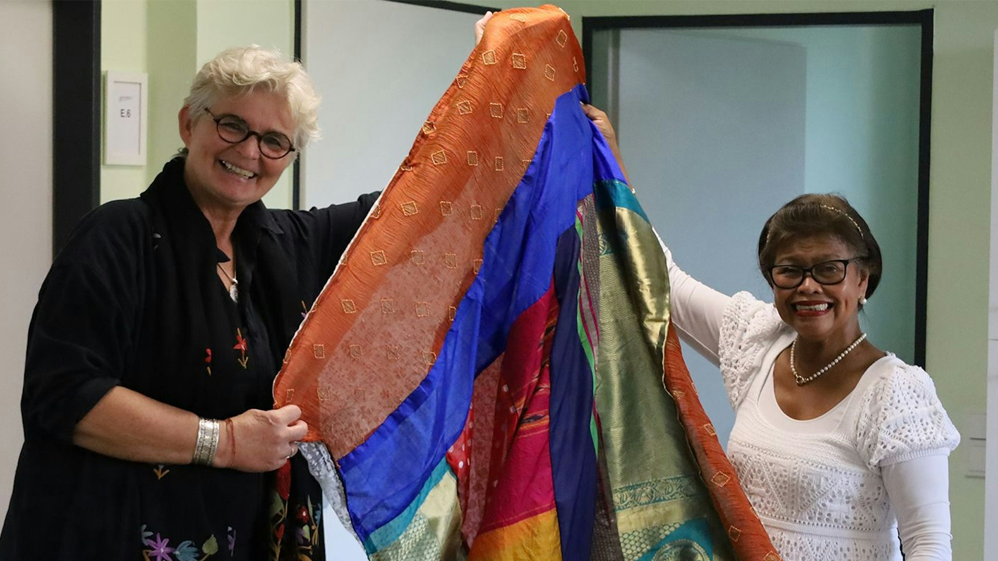 Zwei Frauen der Hennefer Patchwork-Gruppe halten einen Vorhang aus farbigen alten Saris hoch.