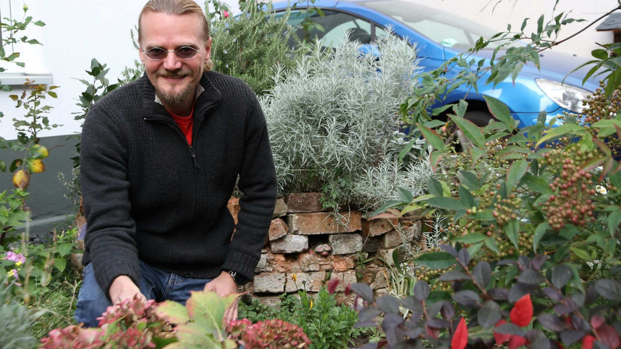 Ein Mann mit getönter Brille kniet vor einer Kräuterspirale.