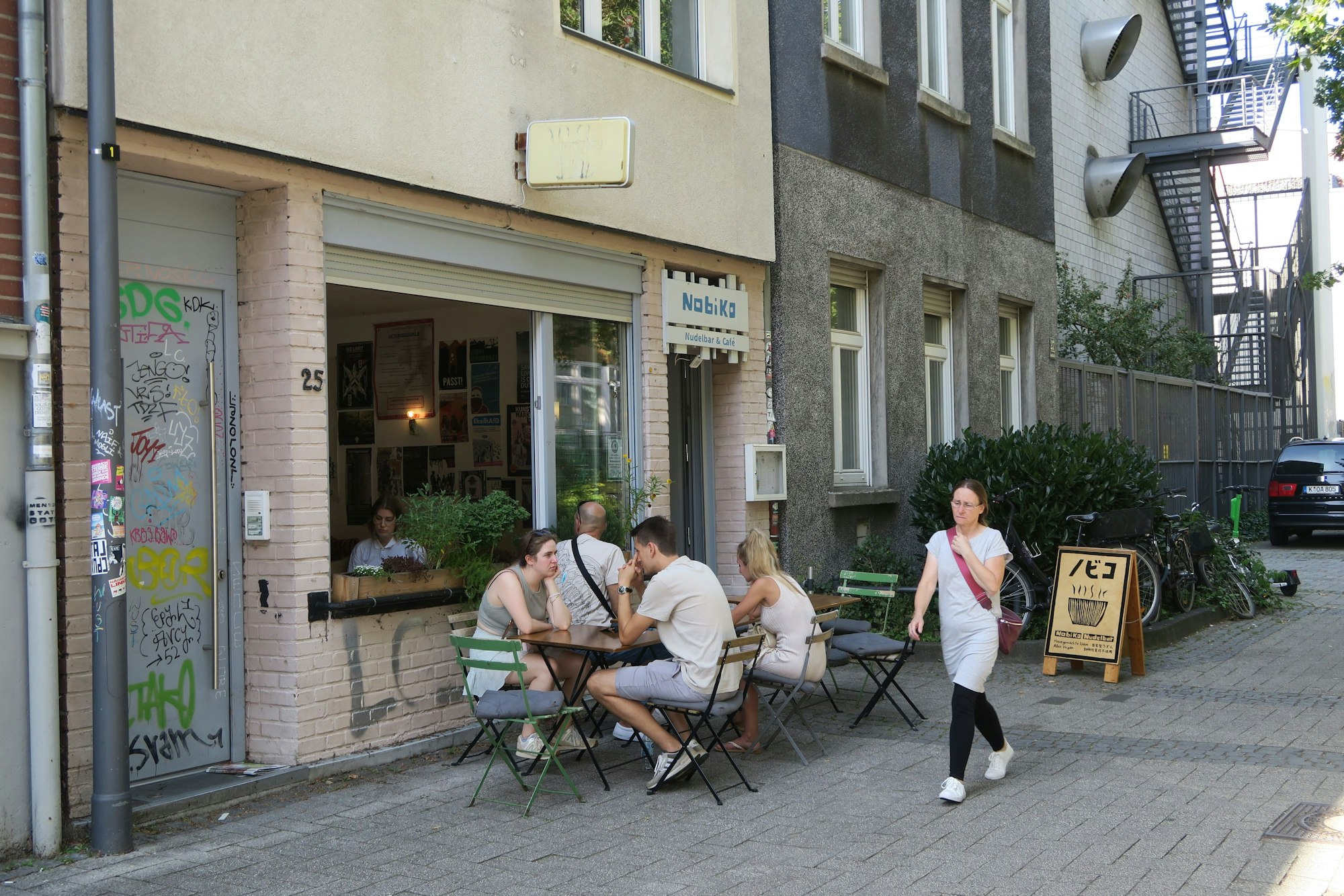 Vor einem Restaurant sitzen Menschen an Tischen.