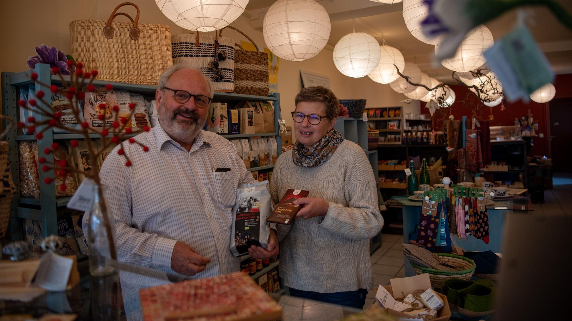 Joachim Berg und seine Frau Bettina Berg-Linde stehen im Verkaufsbereich des Fair-Cafés in Zülpich und präsentieren Kaffee und Schokolade.