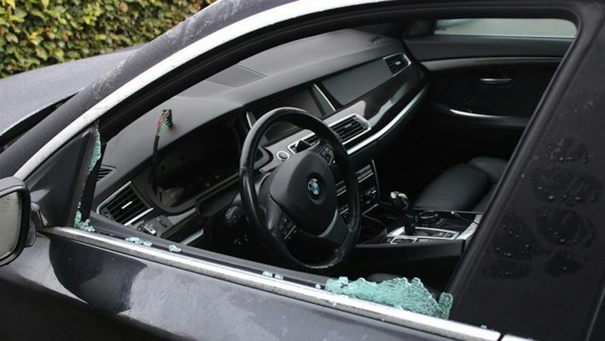 Eine eingeschlagene BMW-Fahrertür von der Seite. Scherben sind im Fensterbereich zu sehen, mittig das Lenkrad des Autos.