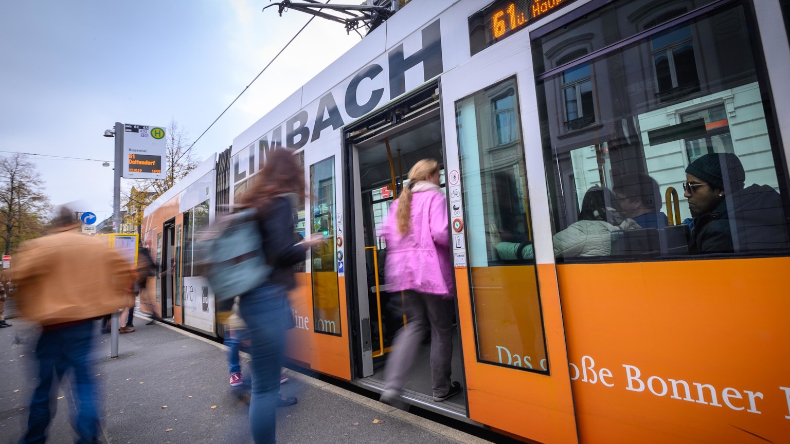 Eine Frau in einer rosa Jacke steigt an einer Bahnhaltestelle in eine Bahn der SWB ein. Weitere Personen am Bahngleis sind nicht erkennbar. Ein Mann schaut rechts im Bild aus dem Bahnfenster.