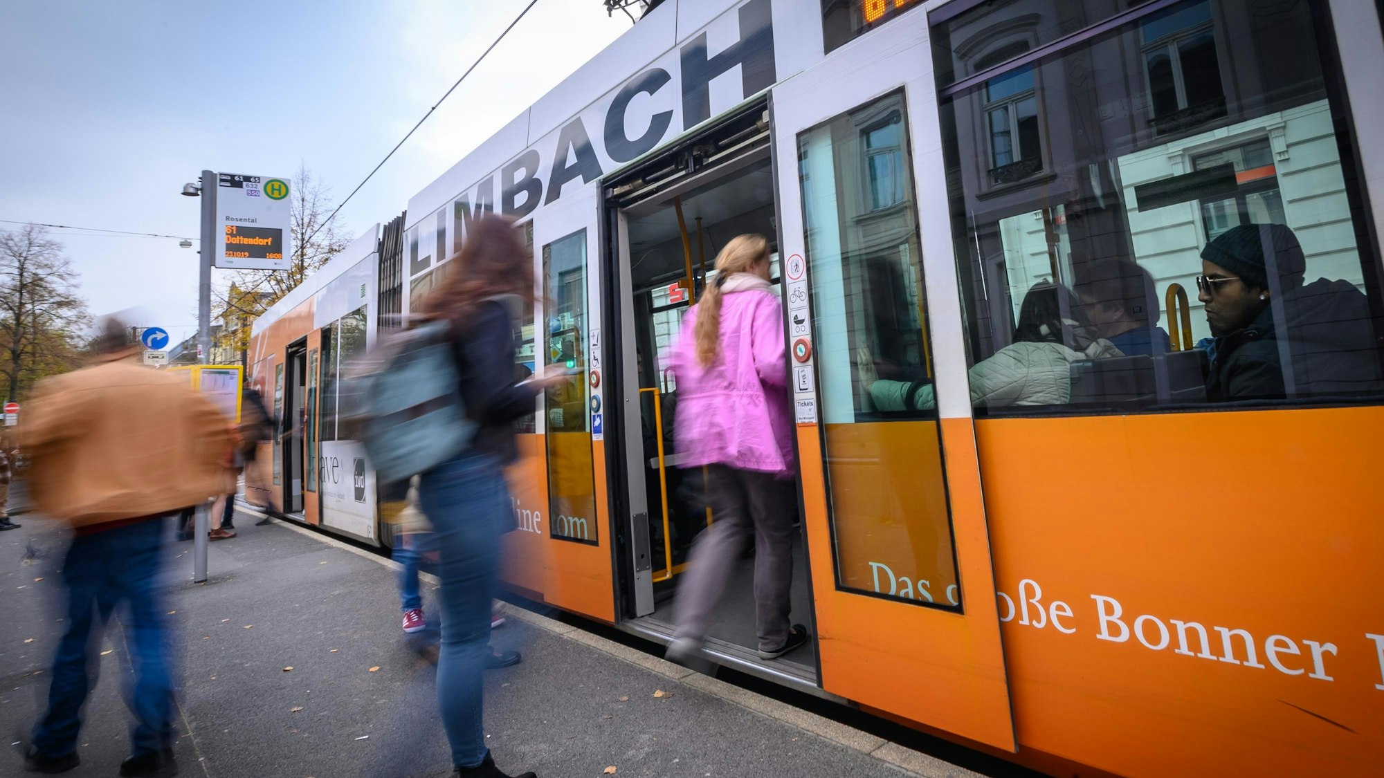 Eine Frau in einer rosa Jacke steigt an einer Bahnhaltestelle in eine Bahn der SWB ein. Weitere Personen am Bahngleis sind nicht erkennbar. Ein Mann schaut rechts im Bild aus dem Bahnfenster.