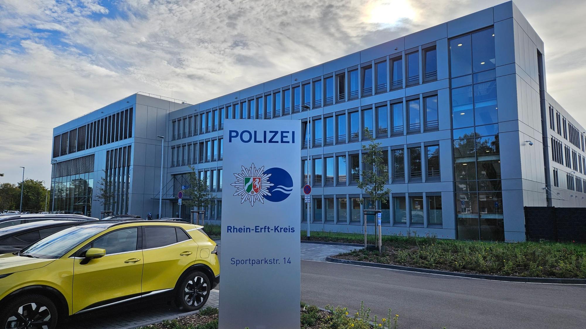 Ein würfelförmiger Bau in Glas und Grau, davor steht ein Schild mit der Aufschrift Polizei.