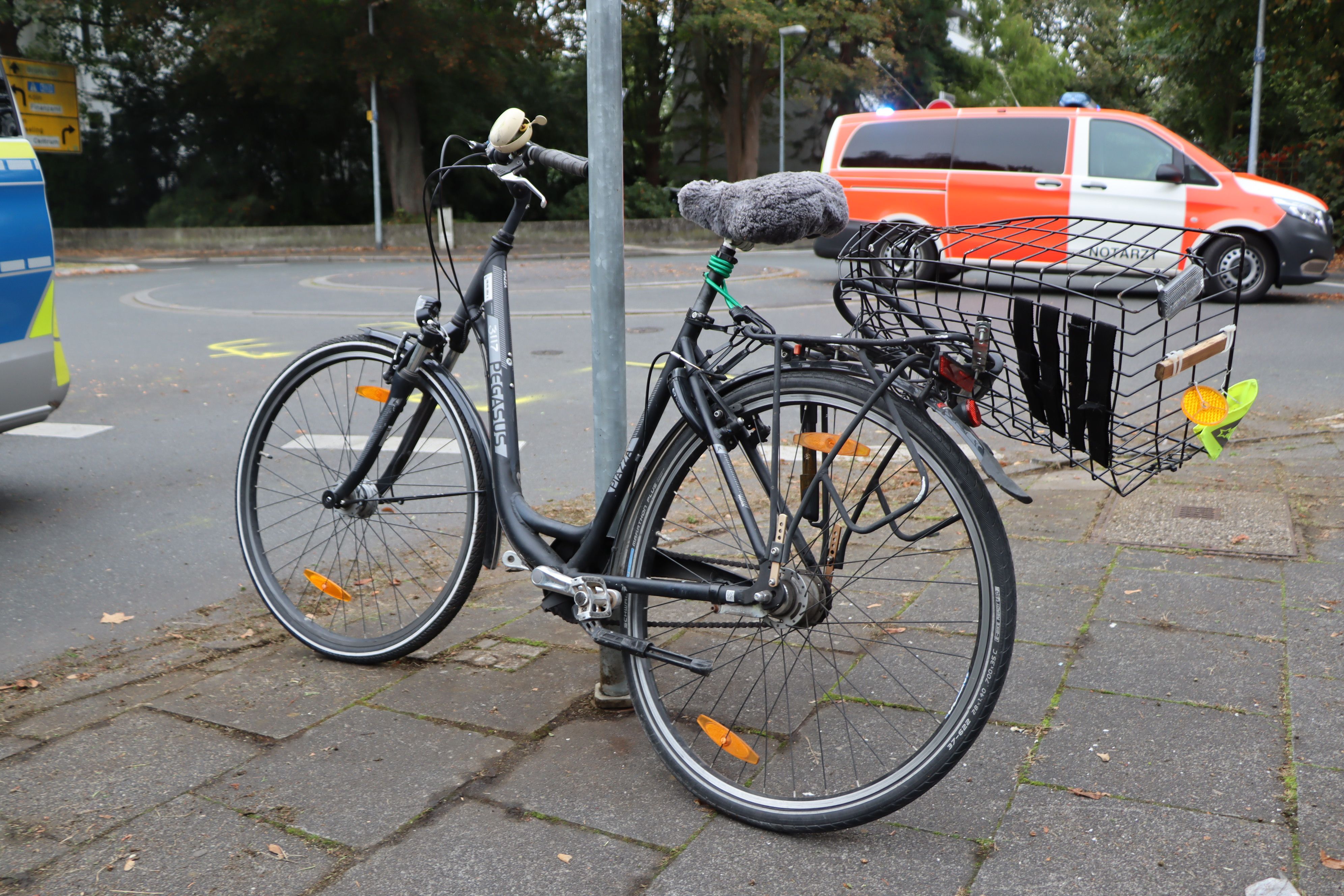 Ein dunkles Fahrrad steht gelehnt an einen Schildpfosten am Kreisverkehr der Brühler Kaiserstraße. Das Rad ist durch den Unfall verbogen.