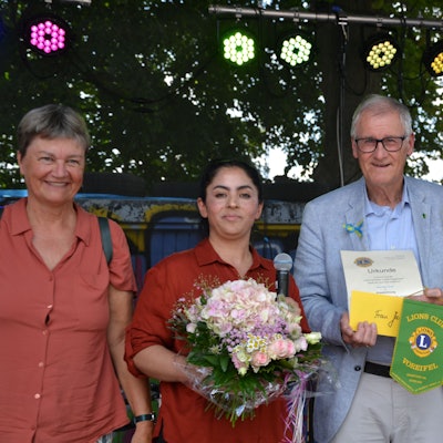 Eine Frau bekommt einen Blumenstrauß und eine Urkunde überreicht.