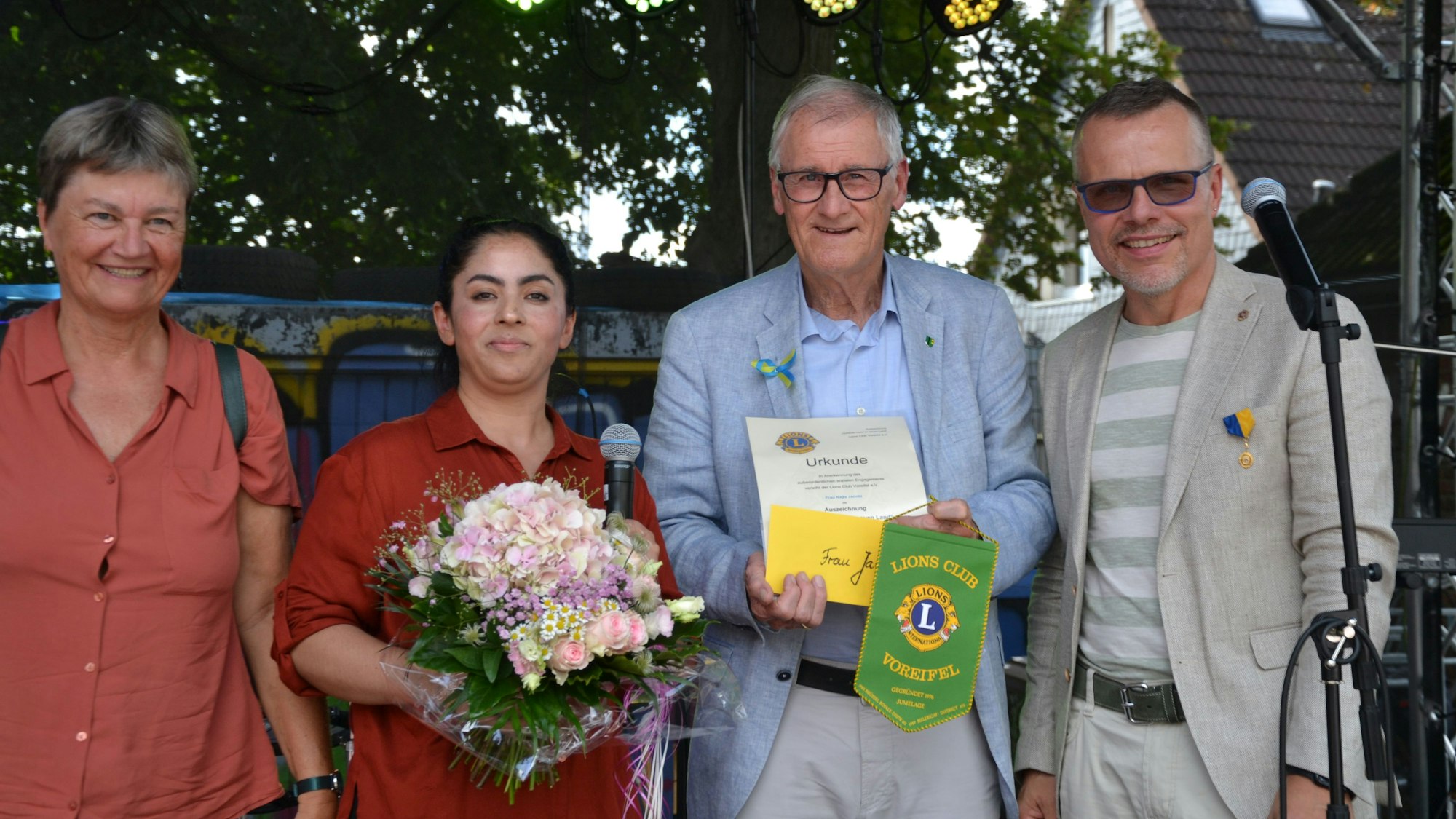 Eine Frau bekommt einen Blumenstrauß und eine Urkunde überreicht.