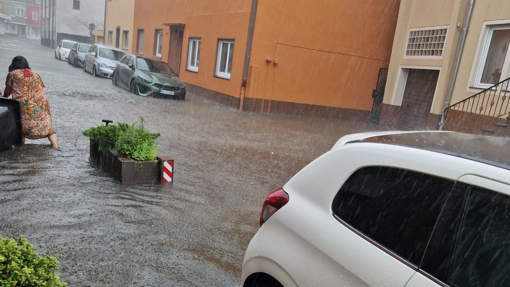 Eine Frau watet durch eine überflutete Straße, Autos stehen im Wasser.