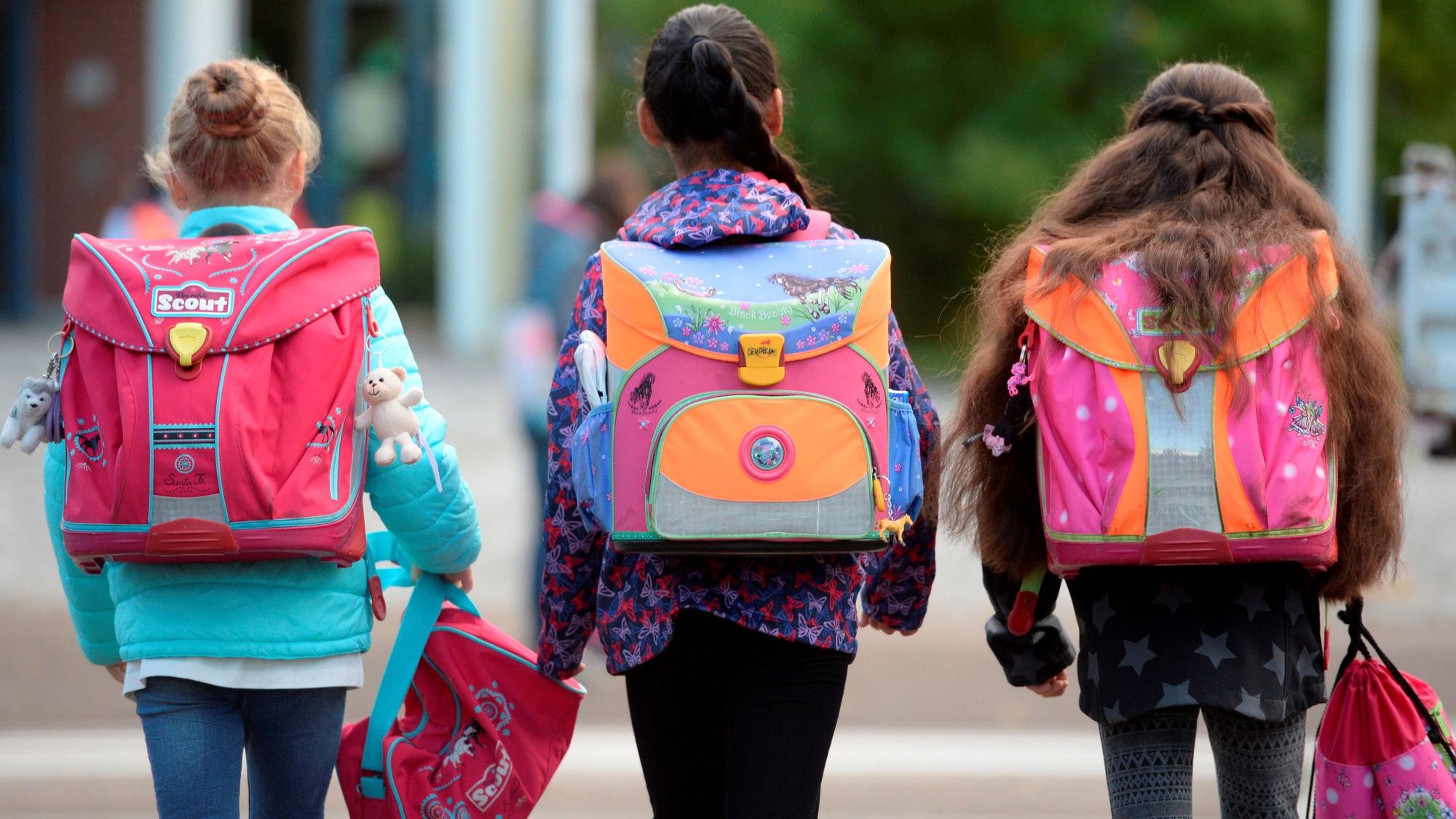 Das Symbolbild zeigt drei Kinder mit ihren Schulranzen auf dem Rücken.