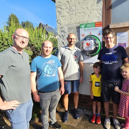 Um den Defibrillator stehen von links Ingo Pfennings, Christian Larres, Stefan Groß, Jesko Priewe mit Tochter und Sohn sowie Oliver Müller.