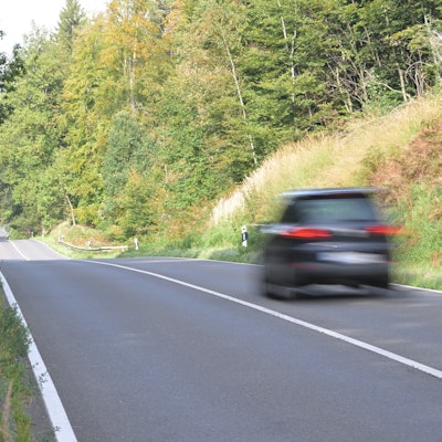 Ein Auto fährt über eine Landstraße, daneben fährt ein Fahrrad auf einem Radweg.