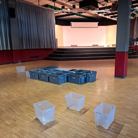 Auf dem Fußboden der gesperrten Aula des Kopernikus-Gymnasiums stehen rund ein Dutzend Plastikbehälter, die das Wasser auffangen, das durch das Flachdach ins Gebäude eindringt.