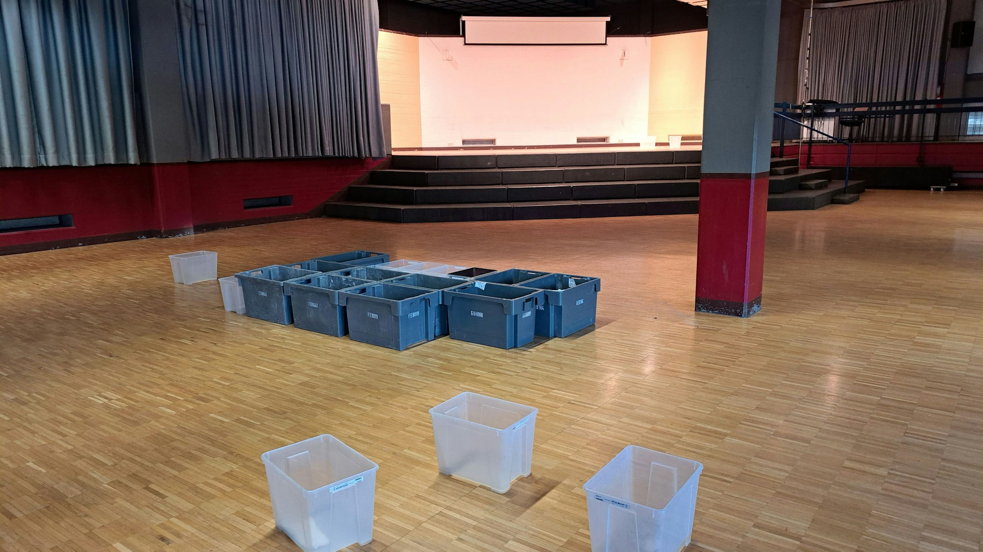 Auf dem Fußboden der gesperrten Aula des Kopernikus-Gymnasiums stehen rund ein Dutzend Plastikbehälter, die das Wasser auffangen, das durch das Flachdach ins Gebäude eindringt.