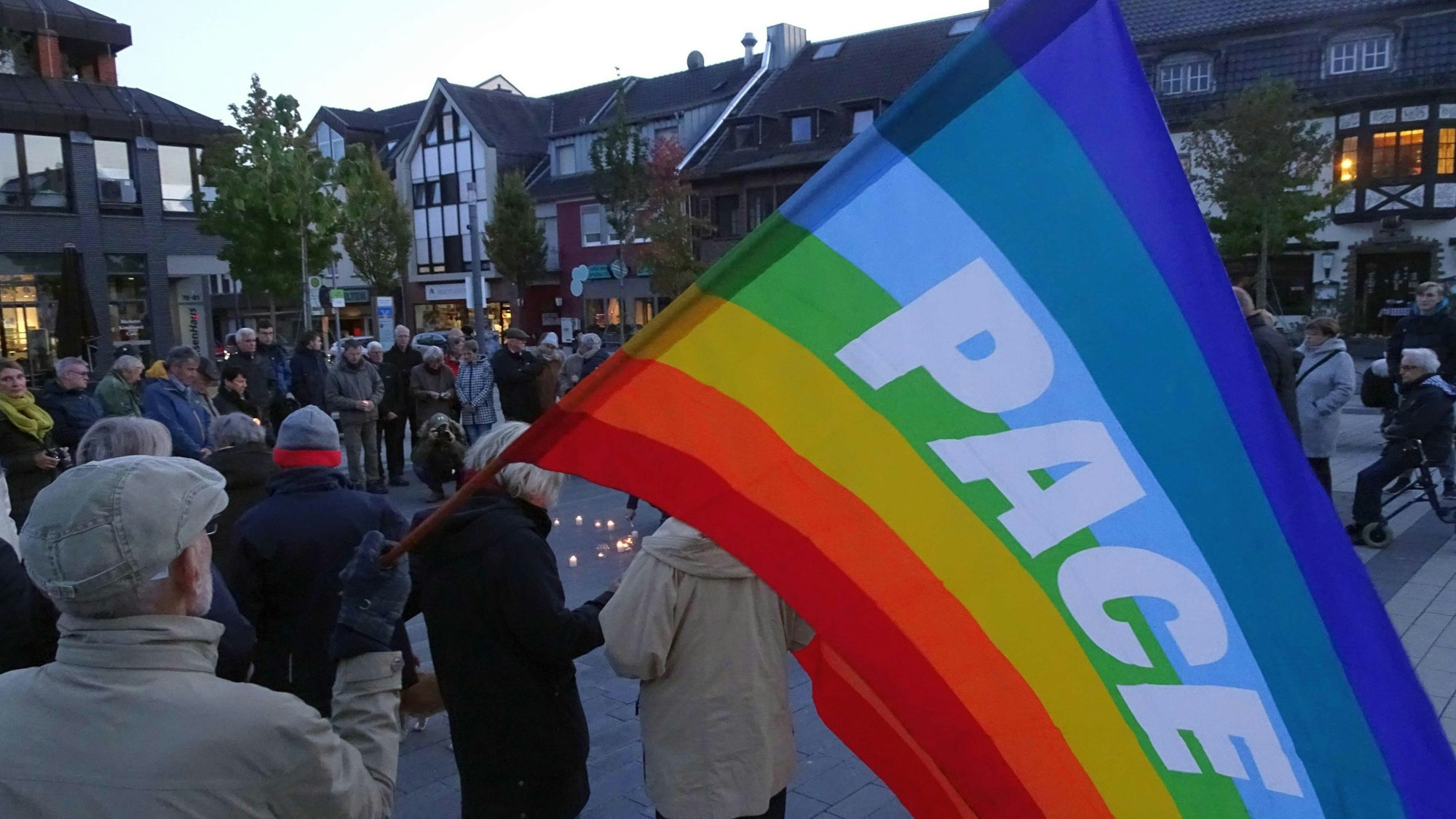 Frauen und Männer stehen auf der Straße. Eine Regenbogenfahne mit der Aufschrift Peace ist deutlich zu sehen.