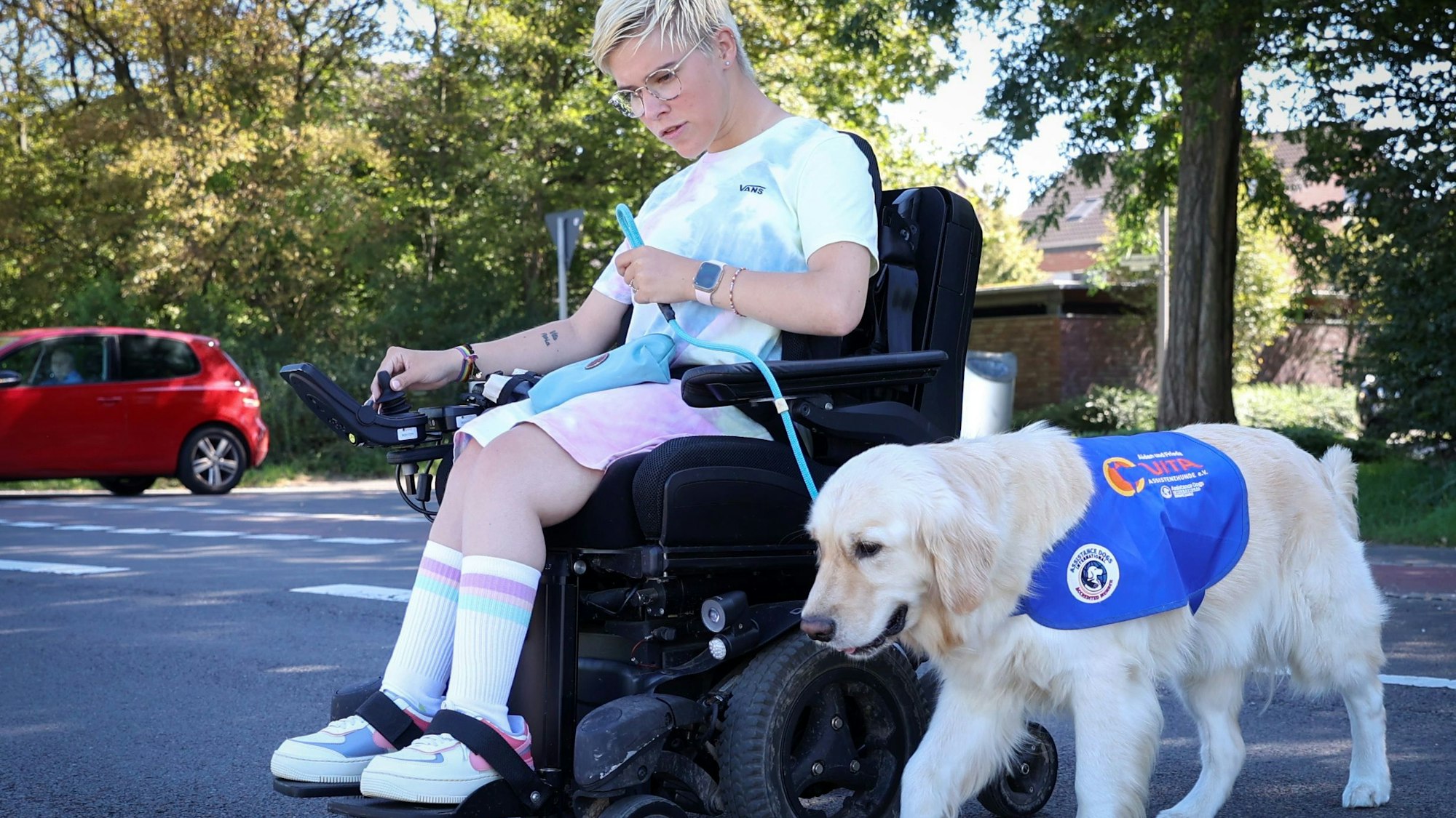 Frieda Krieger fährt im Elektrorollstuhl mit ihrem Assistenzhund Aidan spazieren.