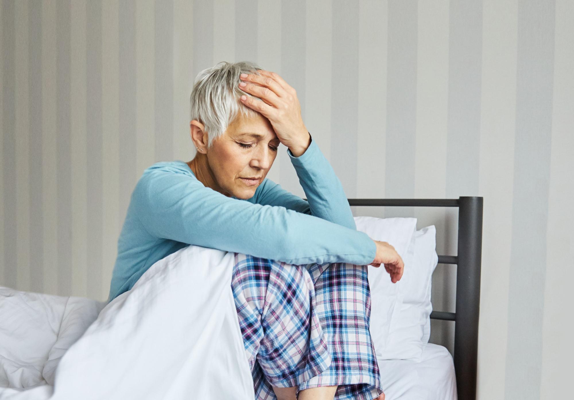 Portrait of an upset and unhappy senior elderly woman with problems or in pain or headache in bed in the morning, a mature woman at home, bedding pillow and sheet