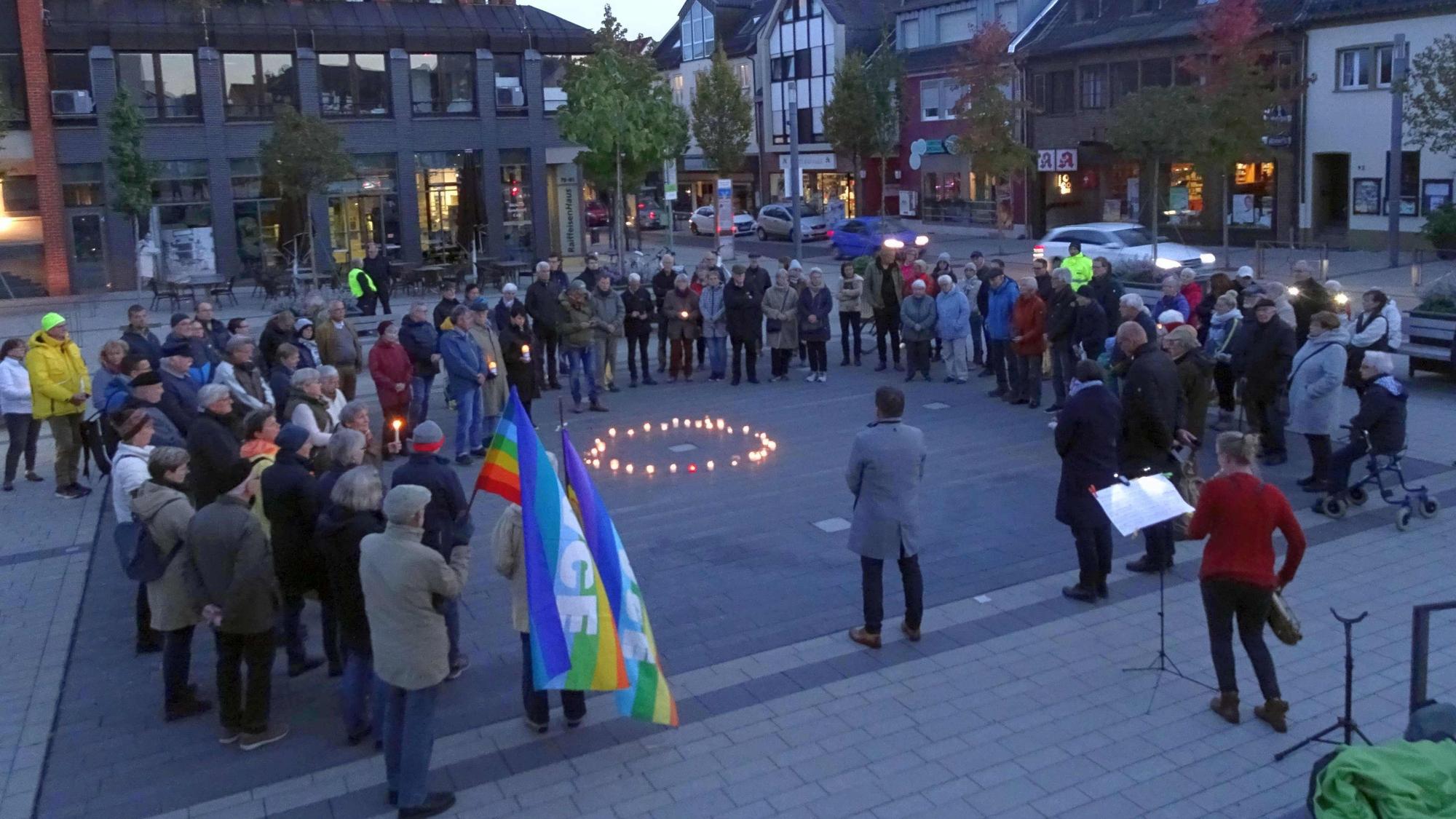 Leute stehen im Halbkreis um einen Kreis, der aus Kerzen besteht.