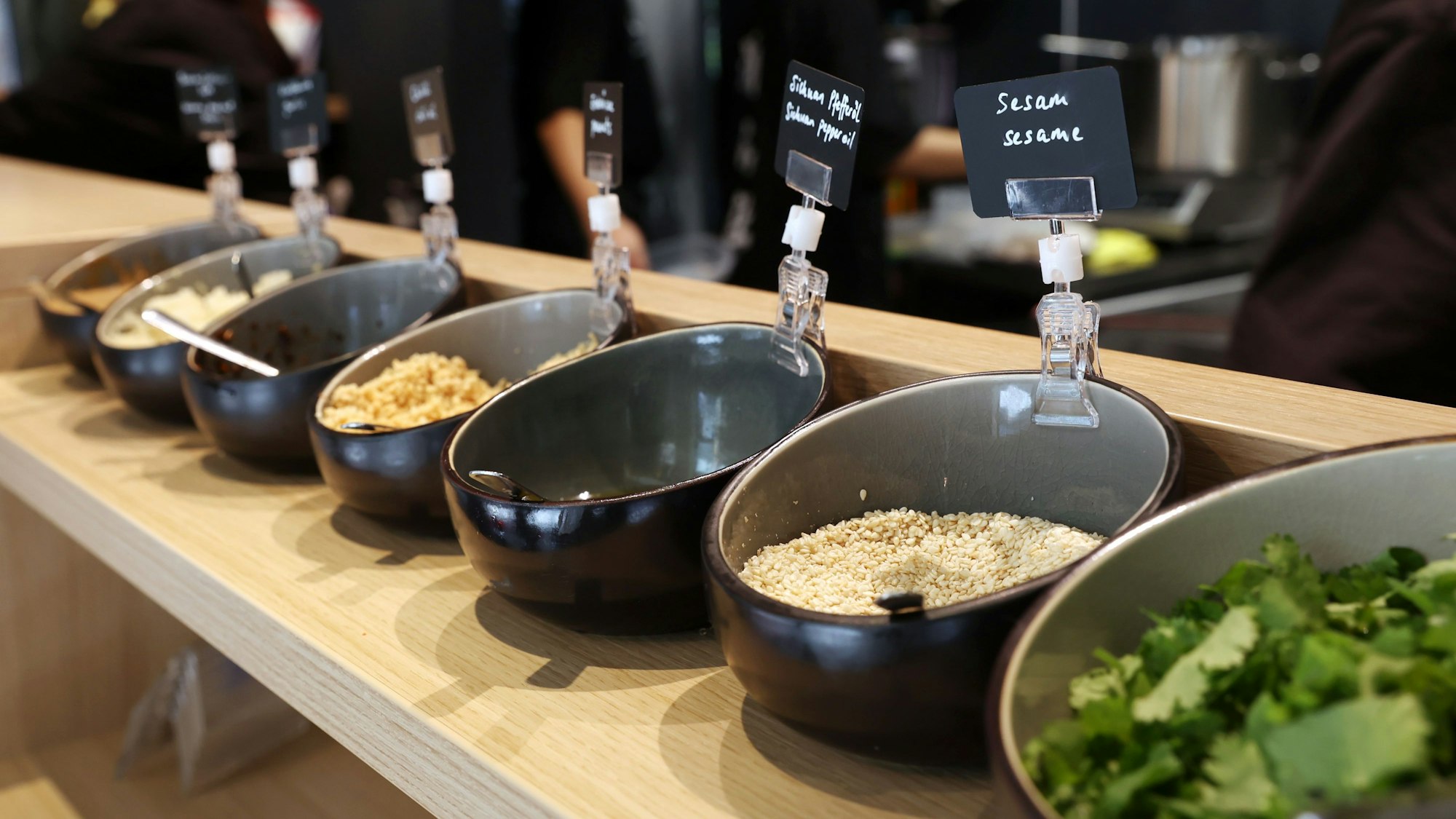 Sesam und weitere Zutaten stehen in Schalen nebeneinander in einem Regal
