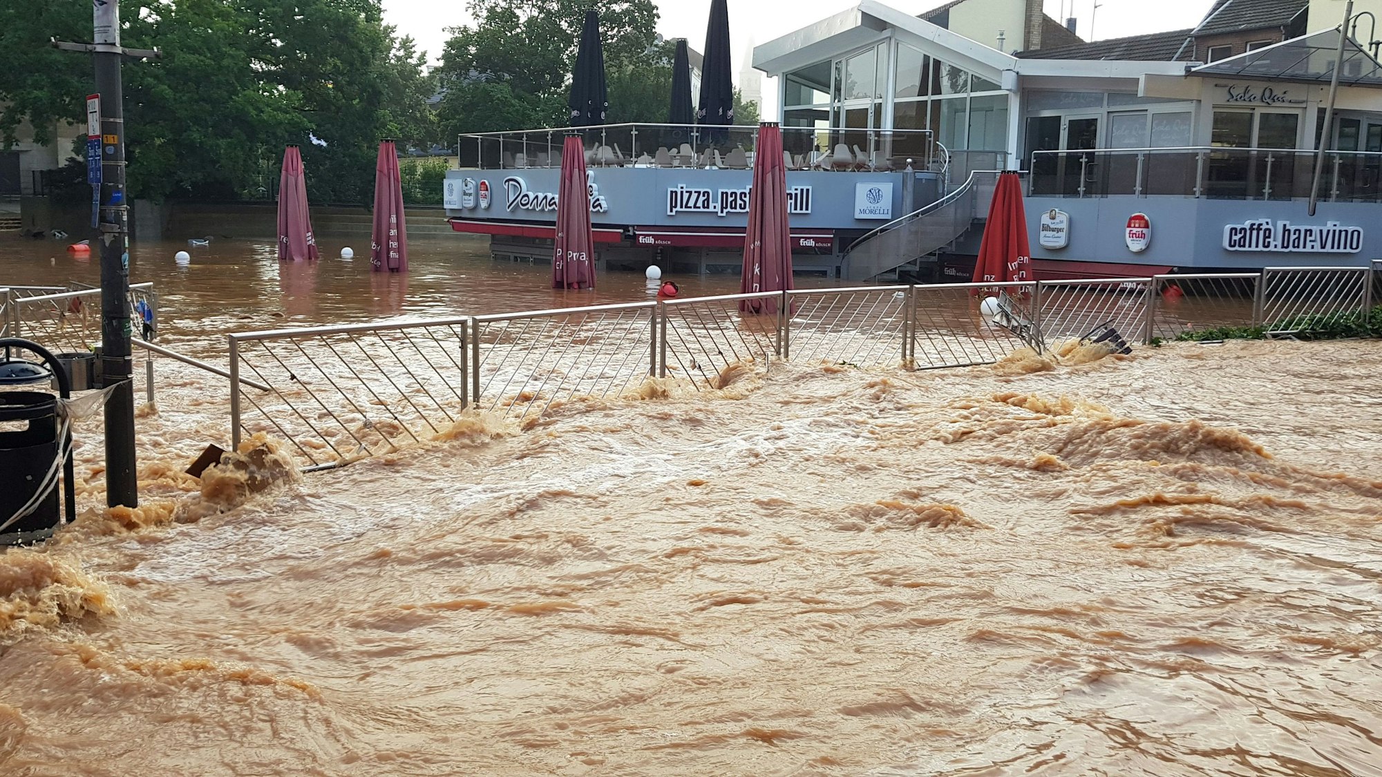 Eines der Ausstellungsbilder zeigt die mit braunem Wasser überflutete Neustraße und den tieferliegenden, vollgelaufenen Herz-Jesu-Vorplatz in Euskirchen.