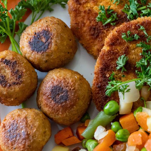 Falafel, vegane Schnitzel und Gemüse liegen garniert mit Petersilie auf einem Teller.