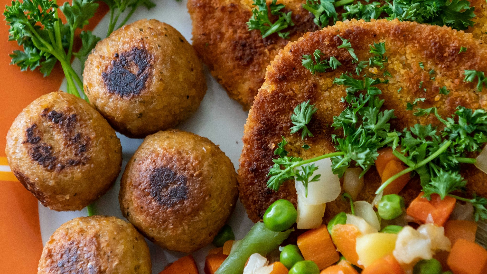 Falafel, vegane Schnitzel und Gemüse liegen garniert mit Petersilie auf einem Teller.