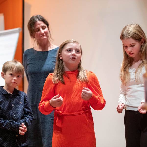 Ein Mädchen hält einen Vortrag, zwei Schulkinder und eine Frau hören zu.