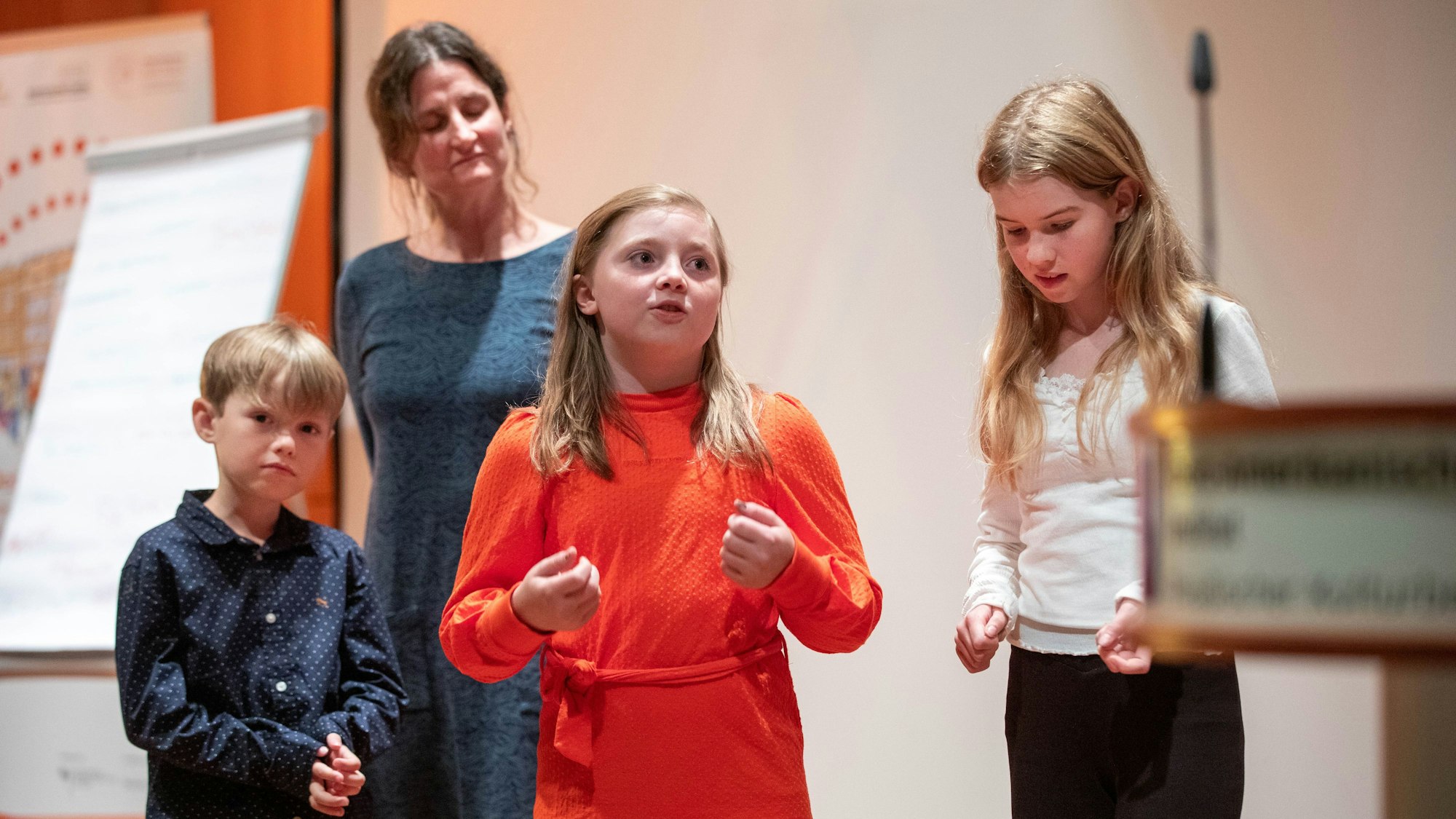 Ein Mädchen hält einen Vortrag, zwei Schulkinder und eine Frau hören zu.