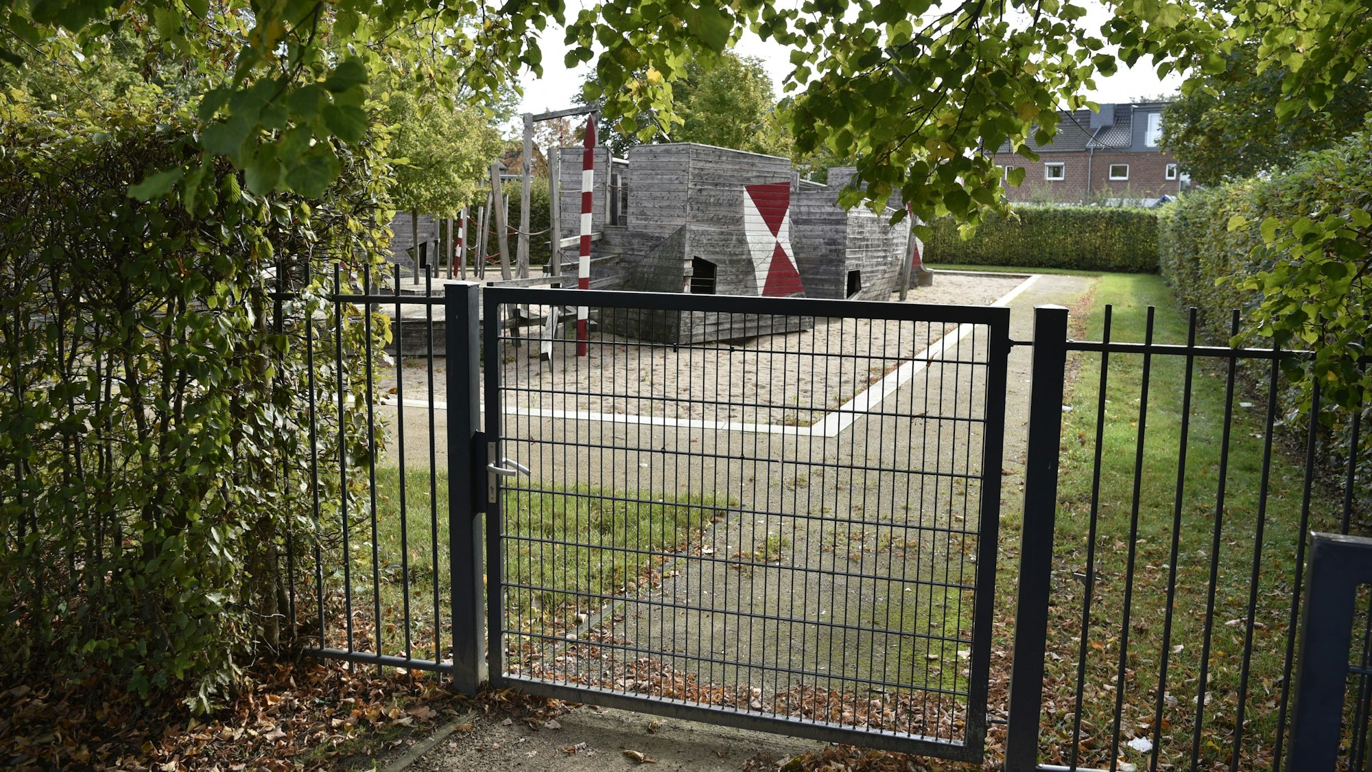 Hinter einem grünen Tor sind Holzspielgeräte eine Spielplatzes zu erkennen.