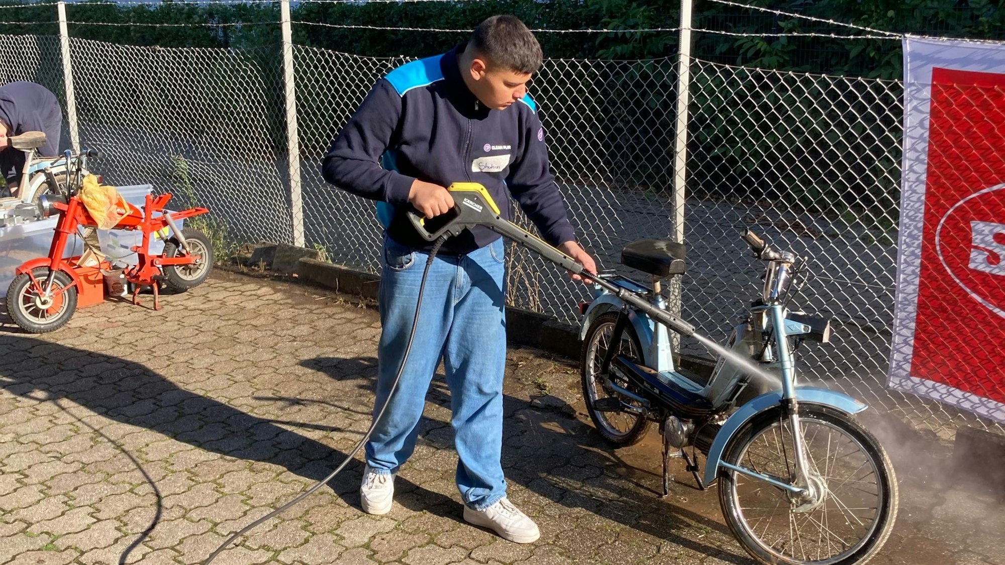 Mit einem Hochdruckreiniger reinigt Schüler Shahin ein Mofa.