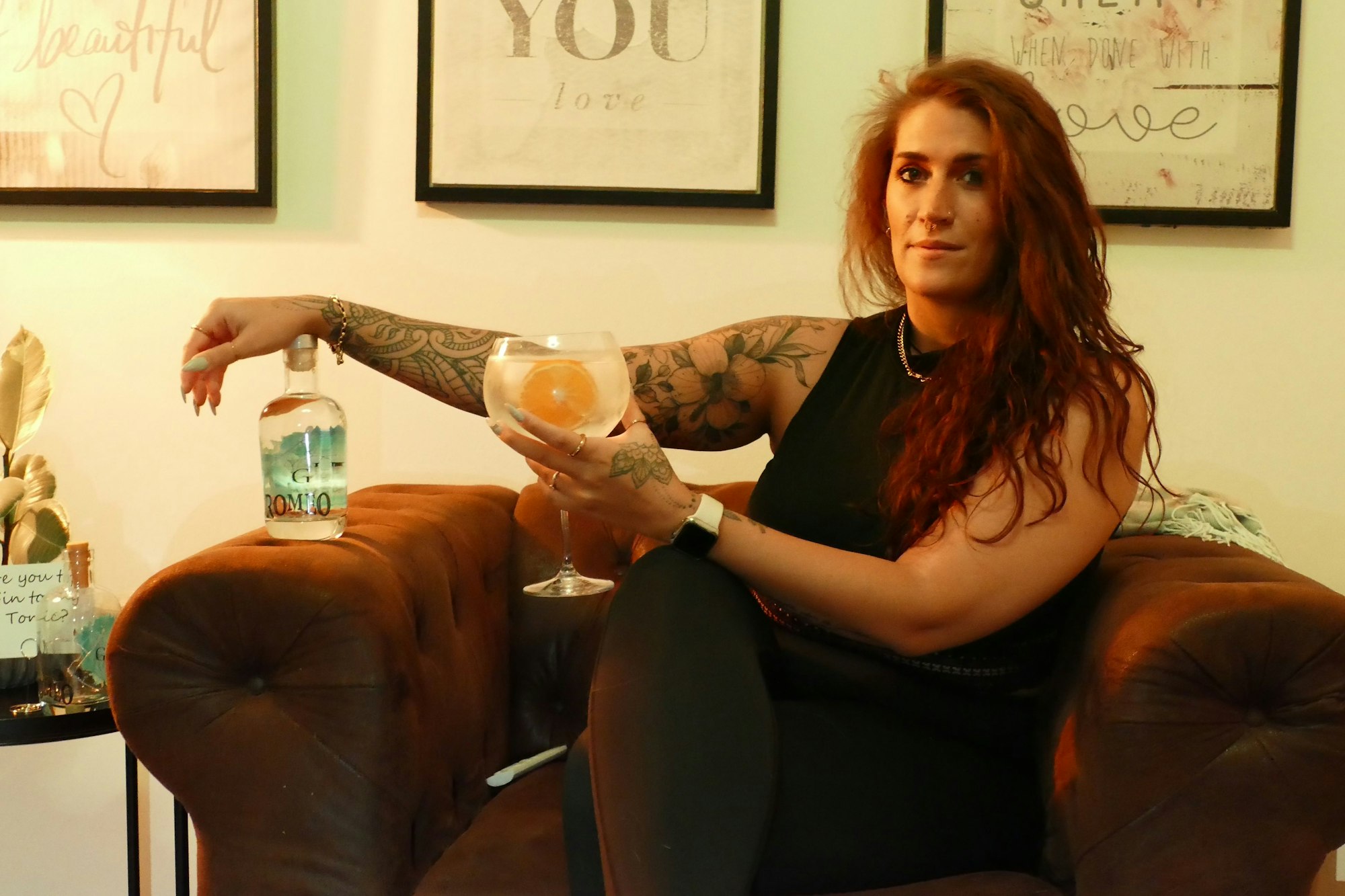 Eine Frau sitzt auf einem Sessel und hält ein Glas mit einem Getränk in der Hand.