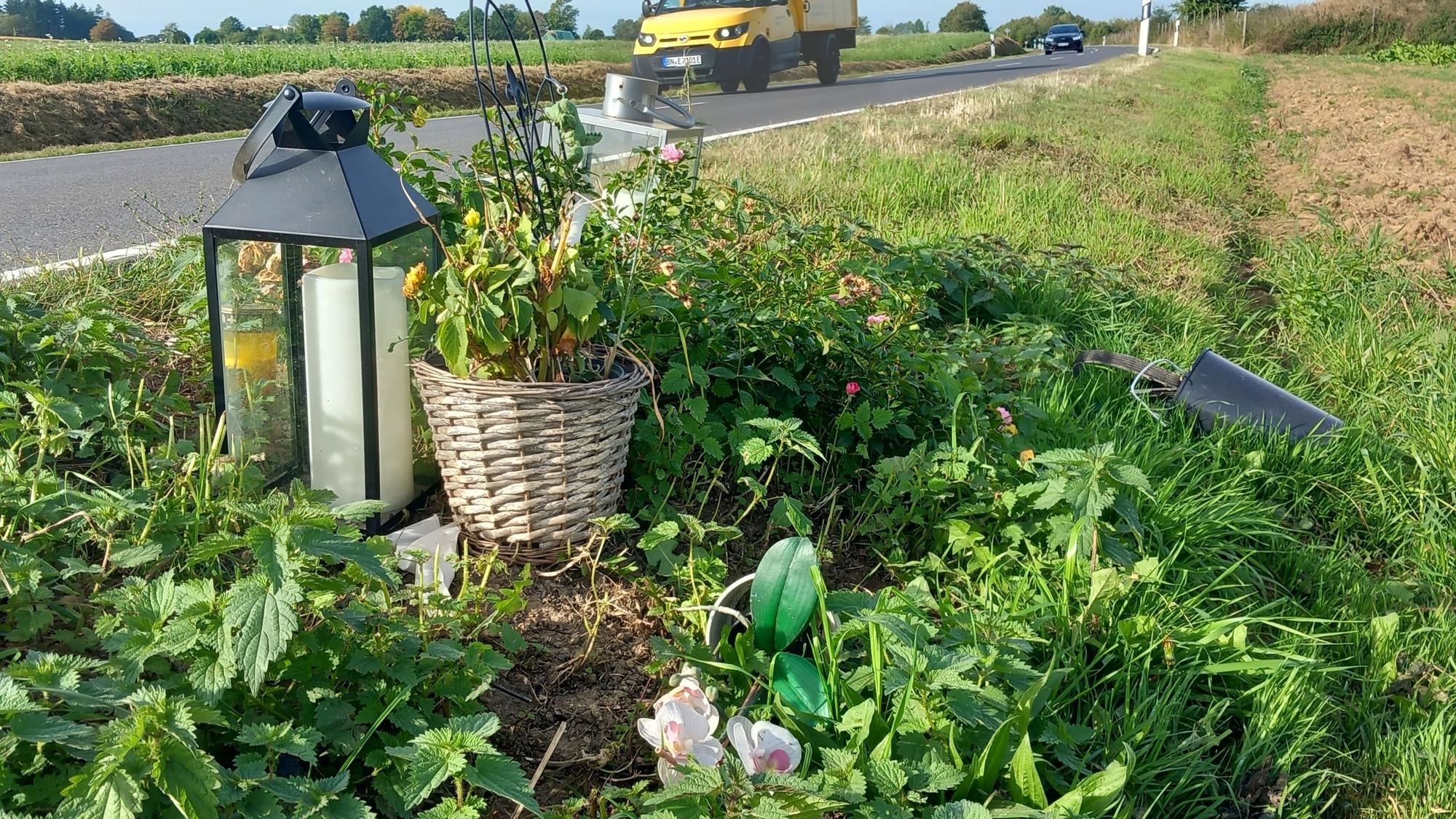 Autos fahren drei Monate nach dem tödlichen Unfall auf der K57 an Kerzen, Blumen und einem Stein vorbei